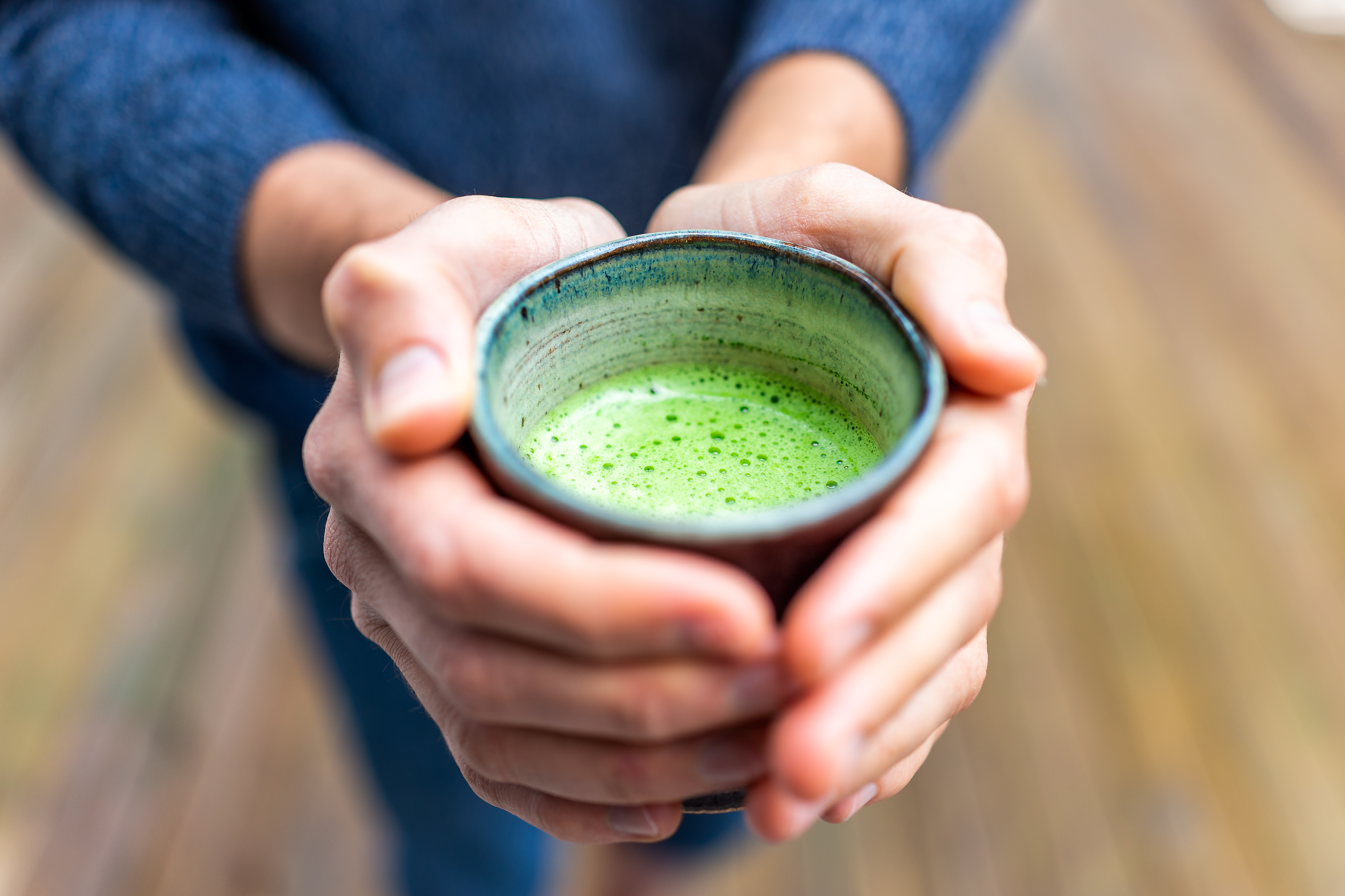 Macro closeup of man person hands holding tea cup outside on backyard deck wooden bokeh background in garden drinking matcha green drink in spring or autumn season
